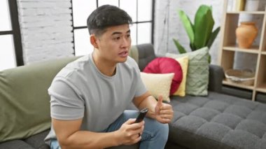 Akıllı telefonlu hevesli bir Asyalı, rahat bir oturma odasında zaferini kutluyor..
