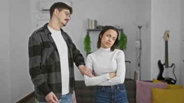 Genç bir adam ve kadın, modern bir oturma odasında karşılıklı şüpheli bir şekilde tokalaşarak karışık duygular paylaşıyorlar..