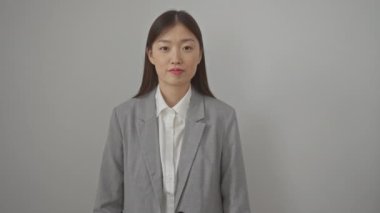 Ceketli genç Çinli bir kadın, dikilip yukarı işaret ediyor. Yüzünde şaşkınlık ve şaşkınlık ifadesi var. İzole edilmiş beyaz bir arka plan.