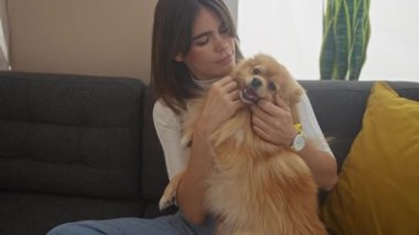 Pomeranian köpeğini sıcak bir oturma odasında şefkatle tutan genç bir kadın evcil hayvan ve sahibi arasındaki bağı gösteriyor..