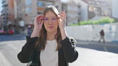 Şehir caddesinde elinde gözlük tutan düşünceli genç bir sarışın kadın portresi.