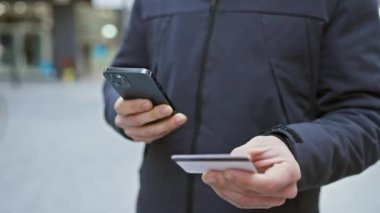 Genç bir adam işlek bir caddede akıllı telefonuyla kredi kartının fotoğrafını çekiyor..