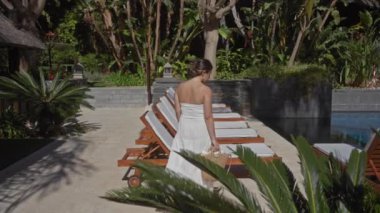 Huzurlu bir tatil köyünde güneşlenen genç bir kadın. Etrafı tropik bitki örtüsüyle çevrili.