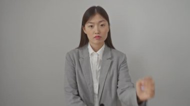 Stresli, ceketli genç Çinli kadın, izole edilmiş beyaz arka planda duruyor, gergin bir şekilde ellerine bakıyor, stres probleminden dolayı tırnaklarını yiyor.