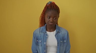 Üzgün Afro-Amerikalı kadın kot gömlek giyiyor, üzgün bir ifadeyle tek başına duruyor, stres ve endişe içinde ağlıyor, izole edilmiş sarı bir arka plan için öfke saçıyor.