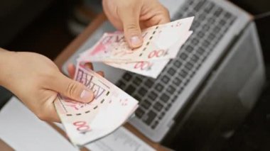 Modern bir iç mekanda Hong Kong dolarlarını dizüstü bilgisayarın üstünde tutan bir adamın yakın plan görüntüsü..