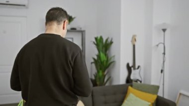 Modern bir oturma odasındaki koltukta akıllı telefon kullanan gevşemiş bir İspanyol..