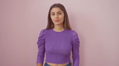 Pembe arka planda duran cahil genç İspanyol kadın. Tişört giyen, güvensiz ve ilgisiz bir tavırla omuz silken şüphesinin şaşkın ifadesi.