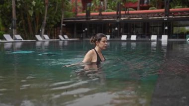 Genç bir kadın, tropik yeşilliklerle çevrili lüks bir bale merkezindeki açık havuzda dinleniyor..