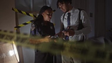 Kadın polis ve erkek dedektif olay yerini akıllı telefon ve rozetle araştırıyor..
