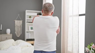 Neşeli orta yaşlı, gri saçlı, pijamasını giymiş, yatak odasının konforunda kendine sevgiyle sarılan, mutluluk ve pozitiflik saçan bir adam..