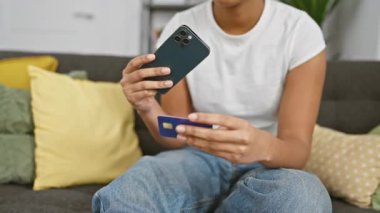 Kanepede akıllı telefon ve kredi kartı kullanan Afrikalı Amerikalı bir kadın.