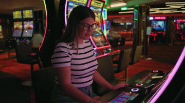 Neşeli genç bir kadın renkli bir kumarhane kumar makinesinde zafer kutluyor, boş zamanlarını ve heyecanı somutlaştırıyor..