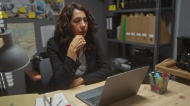 Dedektiflik ofisinde dizüstü bilgisayarı, evrakları ve araştırma çalışmalarını gösteren kanıt duvarıyla yorgun esmer bir kadın.