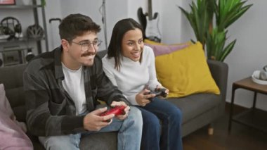 Modern bir oturma odasındaki rahat bir kanepede video oyunu oynayan neşeli bir çift kapalı alanda keyifli bir anı paylaşıyor..