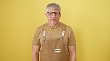 Tüh! Orta yaşlı, gri saçlı bir adam, önlük ve gözlük takıyor, aptalca bir pişmanlıkla el ele tutuşuyor. Kritik bir şey mi unuttun? İzole edilmiş sarı arkaplanda hafıza kaybı. Hatasından rahatsız olmuş..