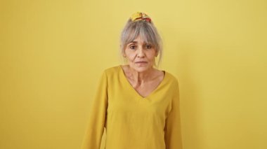 Şok olmuş gri saçlı, orta yaşlı at kuyruklu bir kadın, tamam jest parmaklarının arasından bakarak, inanılmaz bir bakış verir; sarı izole arka planda neşe ile şaşırmış.