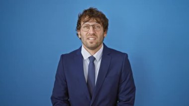 Takım elbiseli, stresli görünen ve gergin elleriyle tırnaklarını yiyen genç bir adam. İzole edilmiş mavi arka planda endişe verici bir sorun.