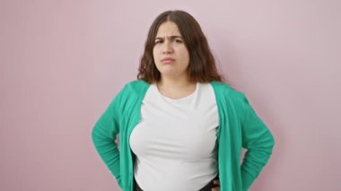 Sinirli bir şekilde dikilen, sorunlara karşı kaşlarını çatan genç Latin bir kadın. Güzel negatif insan şüpheli bir şekilde pembe arka planda izole edilmiş.