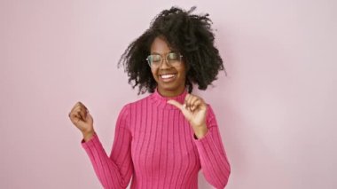 Afro-Amerikalı, kendine güvenen, gözlüklü, mutlu bir şekilde baş parmakları havada, başarı için geriye doğru bakan, pembe iç mekan üzerinde reklam alanı olan,