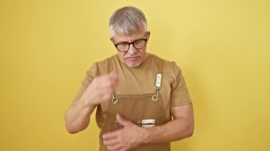 Yorgun, orta yaşlı, gözlüklü, yorgun gözlerini ovuşturan, baş ağrısı ve stresle boğuşan, izole edilmiş sarı arka planda yaşayan gri saçlı bir adam.