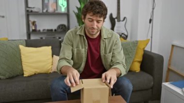 Genç İspanyol bir adam modern bir oturma odasında karton bir kutuyu açıyor..