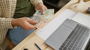 Bir adam, dizüstü bilgisayarın yakınındaki bir marangoz atölyesinde mali işlem portresi yapan Romanya para birimi ley 'i sayıyor..