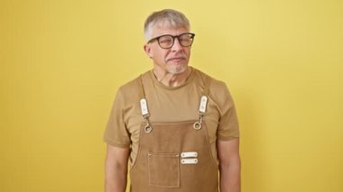 Şşş! Gri saçlı, gözlüklü, orta yaşlı, önlüklü bir adam dudaklarında parmak hareketiyle sessizlik talep ediyor. İzole edilmiş sarı bir arkaplana karşı güvenle duran bir sır saklayıcı..