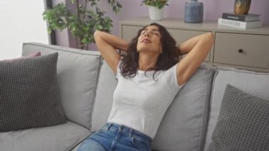 Rahat bir kadın, rahat bir oturma odasındaki kanepede rahat bir şekilde rahat bir şekilde oturuyor, evde boş vakitleri temsil ediyor..