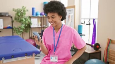 Neşeli Afrikalı Amerikalı kadın zaferini kazanan bir gülümseme, heyecanlı bir ifade ve rehabilitasyon kliniğinde akıllı telefondan kazandığı bir zaferle kutluyor..