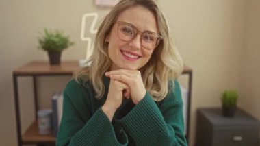 Gözlüklü, rahat bir oturma odasında gülümseyen bir kadın. Öylesine bir zarafet ve sıcaklık yayıyor..