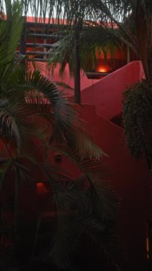 Bali 'de sakin bir alacakaranlık sahnesi. Palmiye yaprakları, kırmızı bir bina ve ince ışıklandırma.