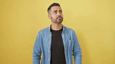 Kot gömlekli, düşünceli, genç İspanyol bir adam. Düşünceli bir tahminle soru soruyor, el pençe divan duruyor. Neşeli bir gülümseme içinde şüpheli bir ifade. Sarı arkaplanda izole bir şekilde duruyor.