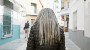 Siyah ceketli, gri saçlı, gülümseyen olgun bir kadın Avrupa 'nın tuhaf bir caddesinde poz veriyor..