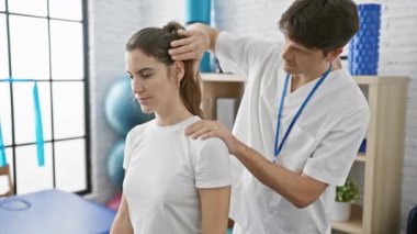 Beyaz önlüklü bir erkek fizyoterapist modern bir fizyoterapi kliniğinde kadın bir hastaya boyun ayarlaması yapıyor.