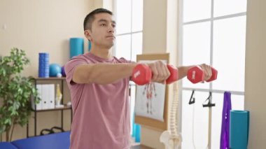 Fizik tedavi kliniğinde dambıllarla egzersiz yapan genç bir İspanyol.