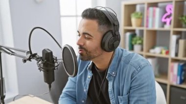 Parlak bir radyo stüdyosunda, kulaklıklı, gülümseyen İspanyol bir adam mikrofona konuşur..