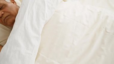 Orta yaşlı bir adam beyaz yatak odasıyla yatak odasında huzur içinde uyuyor..
