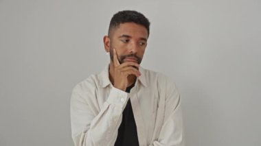 Genç, Afro-Amerikan bir adam, ayakta, gömlek giymiş, düşünceli bir şekilde el pençe üzerinde ciddi bir soru üzerinde kafa yoruyor, izole beyaz bir arka plan üzerinde