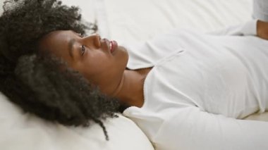 Afro-amerikan kadın baş ağrısı ve ağrısıyla yatağında yatıyor, yatak odasında..