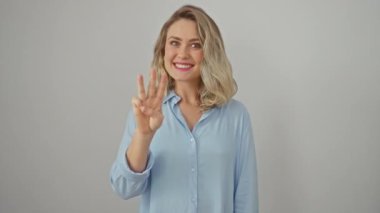 Tişörtlü neşeli sarışın kadın kendinden emin bir şekilde üç parmağıyla işaret ediyor. İzole edilmiş beyaz arka planda üç numaralı işareti mutlulukla gösteriyor.