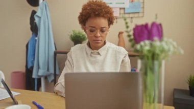 Evde dizüstü bilgisayar kullanan odaklı siyahi kadın modern bir yaşam alanında profesyonelliği ve rahatlığı resmediyor..