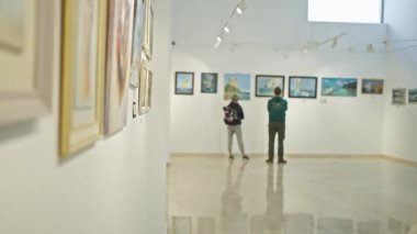 Olgun kadın galeride gözlük ve süveterle sanat yapmayı düşünüyor.