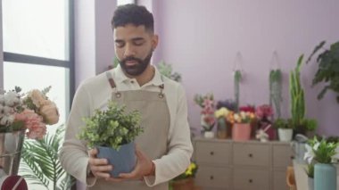 Canlı bir çiçekçide elinde saksı tutan gülümseyen İspanyol bir adam.