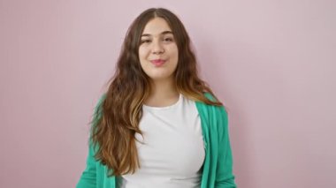 Neşeli, genç İspanyol bir kadın selam veriyor, pembe bir süveterin içinde, izole bir arka planda duruyor. Gülümseyen, gülen, dostça selamlayan, olumlu duygularla dolu bir şekilde merhaba de..