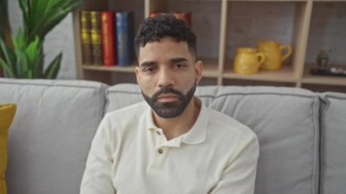 Genç İspanyol bir adam evde, seni şüpheli bir ifadeyle izliyor, gözüne işaret ediyor.