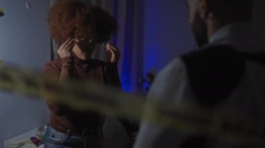 Bir kadın, loş, modern bir oturma odasında, bir diyalog ya da soruşturma hissi uyandıran bir adama açıklar..