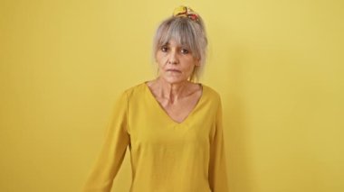 Kendine güveni tam orta yaşlı, gri at kuyruklu bir kadın avucuyla işaret etmeyi kesiyor. Ciddi yüzünde, izole edilmiş sarı arka plana karşı duran bir reddetme işareti var..