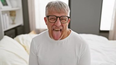 Mutlu orta yaşlı adam, gri saçlı, komik bir ifade takınan, yatak odasında pijama giyen, eğlenen.