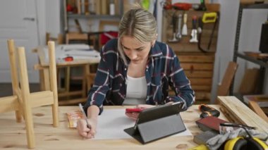 Sarışın bir kadın Filipinli pesoları bir marangoz stüdyosunda tutarken tabletten mali durumları değerlendiriyor..
